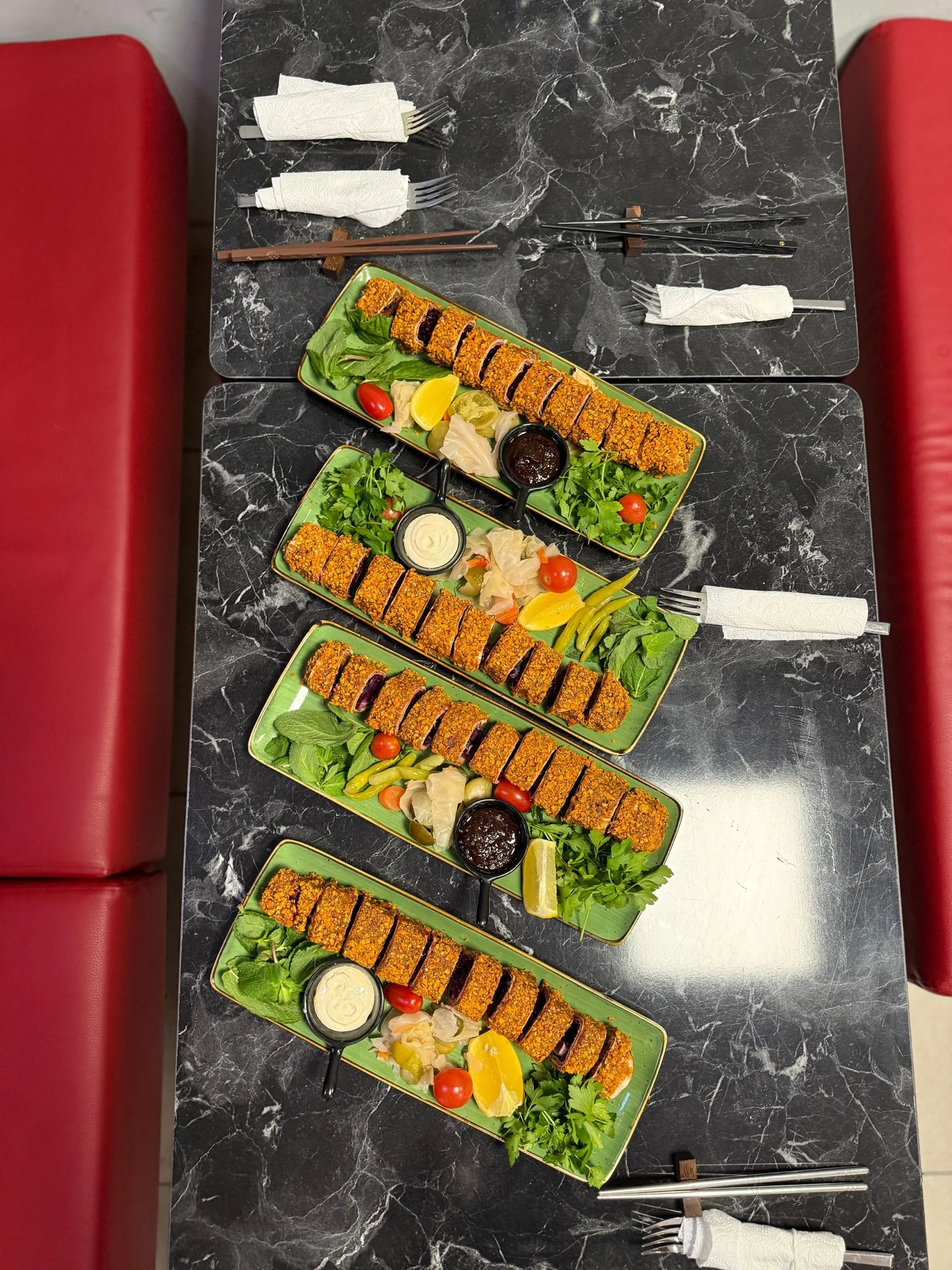 Vier grüne Tabletts mit Sushi-Çiğköfte auf Marmortisch